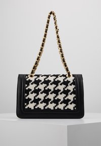Black and white houndstooth-patterned handbag with a black leather base and a gold and black chain strap. Rectangular shape.
