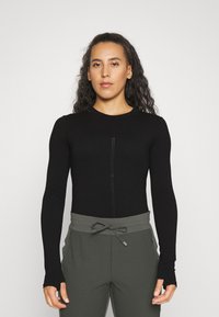 Black long-sleeve top with a round neckline and central seam detail, paired with high-waisted gray pants featuring a drawstring and side pockets.