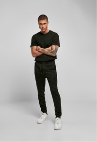 T-shirt noir associé à un jogging noir avec une taille élastique et des coutures sur les côtés. Des baskets blanches complètent la tenue.