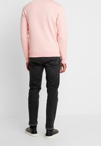 Felpa rosa con scollatura rotonda, polsini e orlo a coste; abbinata a jeans scuri e sneaker nere. Tessuto liscio e vestibilità casual.