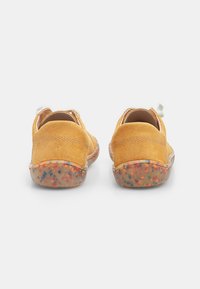 Pantofi din suede galbeni cu vârf rotund, având un spate texturat și o talpă cu pete multicolore. Concepuți pentru confort și ușurință la purtare.