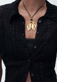 Chemise texturée noire à boutons avec manches courtes, ornée d'un collier pendentif en métal doré en forme de feuille et d'un cordon noir.