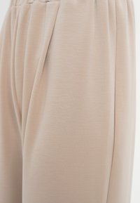 Μπεζ φαρδιά παντελόνια με ελαστική μέση και λεπτομέρεια πλαϊνής τσέπης, εμφανιζόμενα σε κοντινό πλάνο σε απαλό υφασμάτινο ύφος.