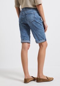 Shorts de mezclilla azul claro con puños enrollados, dos bolsillos traseros y un corte relajado. Presentan una textura suave y ligeramente desgastada.