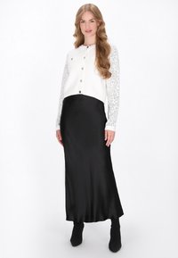 Fehér, rövidített kardigán gombos záródással, csipkés ujjakkal, fekete selyem maxi szoknyával és fekete bokacsizmával párosítva.