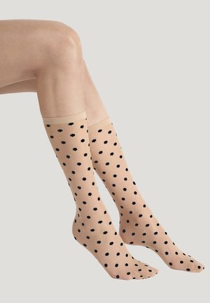 Gambe con calze a rete color carne fino al ginocchio, con piccoli motivi a fiore nero distribuiti uniformemente su uno sfondo chiaro e uniforme.