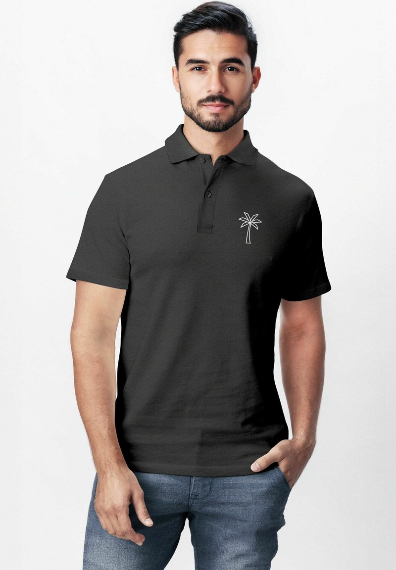 Schwarzes Polohemd mit kurzen Ärmeln, Kragen und einem weißen Palmenemblem auf der linken Brust; kombiniert mit blauen Jeans.
