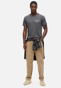 Grå bomulds t-shirt med et vintage print, parret med tan fløjl bukser. En mørk ternet flannel skjorte er bundet om livet. Beige sneakers er iført.