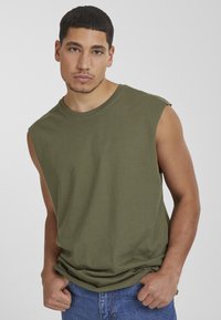 Maglietta senza maniche verde oliva realizzata in cotone morbido, con scollatura rotonda, vestibilità comoda e dettagli di pieghe sottili sulle spalle.