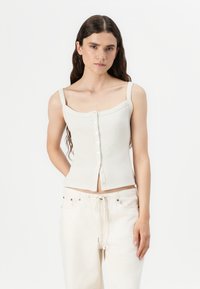 Ribbed, off-white crop top with straight neckline, thick straps, and front button closure. Smooth texture with fitted silhouette.