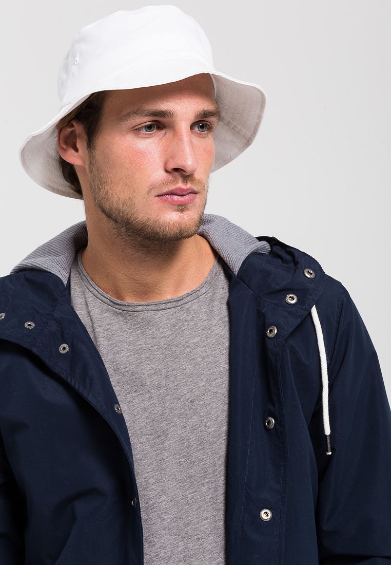 White bucket hat on a man wearing a navy jacket with a grey shirt. The jacket has a double zipper and grey collar lining.
