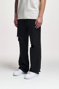 Svart denim jeans med store hull ved knærne, løs passform, kombinert med hvite sneakers og en lys farget t-skjorte.