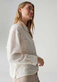 Camicia bianca con bottoni, tessuto strutturato, dettagli sfrangiati, maniche lunghe e collo con bottone. Tessuto liscio con vestibilità rilassata.