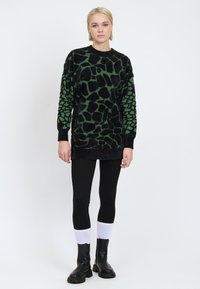 Schwarzer und grüner strukturierter Pullover mit gemustertem Design. Tragen mit schwarzen Leggings und schwarzen Stiefeletten mit weißen Akzenten.