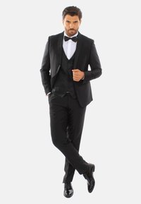 Tuxedo nero con accenti in raso, camicia bianca, cravatta a farfallino e scarpe lucide nere. La vestibilità su misura mette in risalto un design classico.
