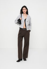 Γκρι cropped πλεκτή ζακέτα από μείγμα μαλλιού με διπλή σειρά κουμπιών, συνδυασμένη με καφέ παντελόνια φαρδιάς γραμμής και μαύρη δερμάτινη τσάντα.