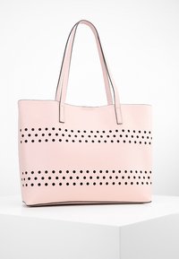 Roze schoudertas van textuurmateriaal met horizontale rijen van zwarte ronde uitsneetjes, voorzien van stevige handvatten en een strakke, minimalistische stijl.