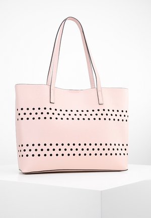 Sac fourre-tout rose en matériau texturé présentant des rangées horizontales de découpes circulaires noires, avec des poignées robustes et un design épuré et minimal.