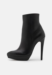 Černá kožená kotníková bota s špičatou špičkou, vysokým stiletto podpatkem a platformovým siluetou. Hladká textura a minimalistický design.
