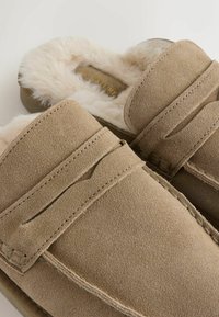 Svetlohnedé semišové mokasínové papuče s umeelou mäsovou podšívkou a detailným prešívaním. Štýl na obúvanie s jemnou textúrou a nenápadným označením.