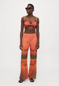Conjunto de bañador de dos piezas que incluye un top sin tirantes con nudos en color coral, con detalles de palmeras y acentos en naranja; pantalones anchos a juego con estampado de atardecer.