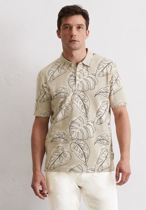 Beige short-sleeve polo shirt with a ribbed texture and black tropical leaf pattern. Features a classic collar and three-button placket.