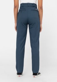 Marinblå byxor med hög midja, två bakfickor och ett strukturerat tyg. Har en logotypnuva och rak benstil.