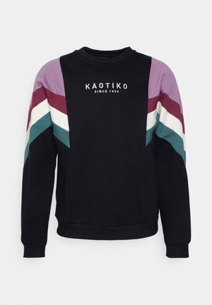 Schwarzer Sweatshirt mit Rundhalsausschnitt und violetten, burgunderfarbenen, weißen und türkisfarbenen Chevronstreifen an den Ärmeln sowie dem Schriftzug „KAOTIKO SINCE 1999“ auf der Brust.