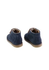 Botas de tobillo de ante azul marino con cordones marrones, parte trasera redondeada, detalles texturizados y suela de goma en contraste.