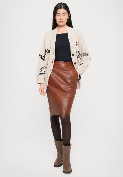 Cardigan beige lavorato a maglia con ricami, top nero, gonna a matita in pelle marrone, collant marroni e stivali alla caviglia grigi. Design semplice e aderente.