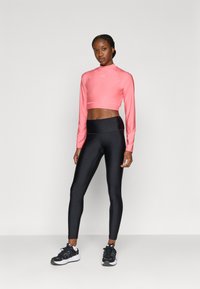 Ροζ φωτεινό crop top με μακριά μανίκια, εφαρμοστά μαύρα κολάν και μαύρα αθλητικά παπούτσια. Το υλικό φαίνεται λείο με ελαστική υφή.