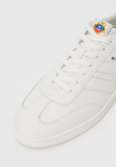 Adidași din piele albă, cu vârf rotund, suprafață texturată, șireturi plate și un logo pe limbă. Prezintă cusături subtile și o talpă de profil joasă.