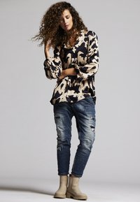 Lässiges, beige und marineblau gemustertes Oberteil mit übergroßen Ärmeln, kombiniert mit ausgewaschenen Jeans und beigen Ankle Boots.