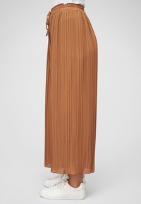 Pleated, mid-length skirt in a warm brown tone, made from lightweight fabric. Features an elastic waistband with a drawstring detail.