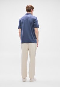 Tmavomodré polo tričko s krátkymi rukávmi, jednoduchý dizajn, bavlnený materiál, v kombinácii so svetlobéžovými nohavicami, hladká textúra a pohodlný strih.