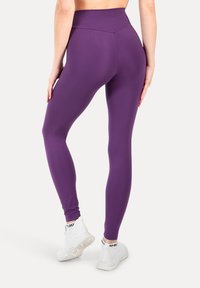 Leggings morados hechos de un tejido elástico, con una cintura alta, textura suave y un diseño ajustado. Llevados con zapatillas blancas.