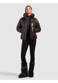 Blank, mörkbrun puffjacka med hög krage, framdragkedja och sidofickor, kombinerad med svarta leggings och blanka svarta vinterstövlar.