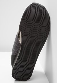 Black shoe featuring a textured rubber sole with wave patterns, a sparkly gray accent across the upper, and smooth leather details.