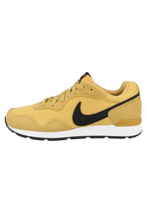 Żółty but do biegania Nike z czarnym logo Swoosh, białymi środkowymi podeszwami i czarnymi zewnętrznymi podeszwami, widziany z boku.