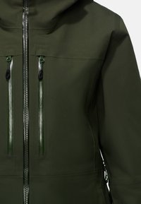 Giacca impermeabile verde con una texture liscia, zip frontale completa e due tasche con zip dotate di accessori neri a contrasto.