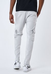 Pantalones cargo de color gris claro hechos de una mezcla de algodón, con bolsillos laterales, un corte ajustado y un diseño de largo hasta los tobillos, combinados con zapatillas blancas.