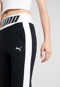 Puma svarta sweatpants har en midja med vit logotyp, vita sidostrick, en liten logotyp på benet och ett mjukt, texturerat tyg.