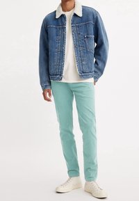 Jeansjacka med fårskinnskrage, ljusblå, knäppning framtill; ihop med mintgröna byxor och vita sneakers. Modell står upprätt.