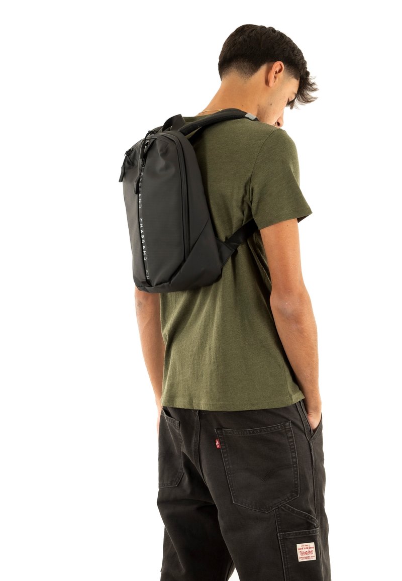 Mochila negra de diseño elegante, con una superficie texturizada y correas ajustables, llevada en la espalda de una persona con una camiseta verde.