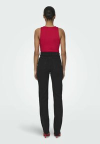 Svarta jeans med hög midja och rak passform, kombinerat med en ärmlös röd topp. Slät tyg, minimalistisk design, inga synliga mönster.
