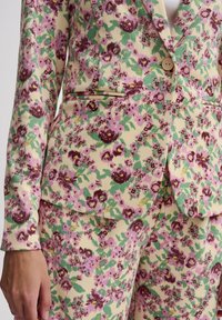 Blomsterblazer og bukser i creme med pink og grønne accenter. Materiale: tekstureret stof. Funktioner inkluderer en enkelt knap og lomme detalje.