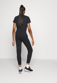 Zwarte atletische top en zwarte joggers met een gespikkeld patroon. De joggers hebben een elastische tailleband en taps toelopende boorden, gecombineerd met zwarte sneakers.