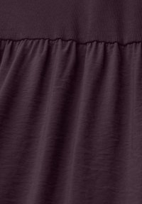 Tissu violet foncé montrant une couture avec une ceinture élastique côtelée joignant un matériau lisse froncé en dessous.