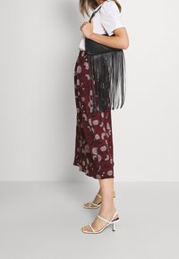 Weinrot gemusterter Midirock mit weißem Blumenmuster, kombiniert mit einer schwarzen Leder-Crossbody-Tasche mit langen Fransen und weißen geschnürten Absatzsandalen.