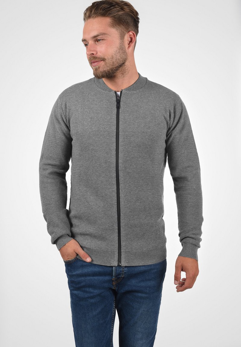 Siva zip-up kardigan iz teksturiranega pletenega materiala, ki ima okrogel ovratnik, rebraste manšete in rob ter kontrastni črn zadrgo.